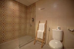 A bathroom with patterned tiles, a glass shower enclosure, a wooden towel rack, and a toilet with a paper towel dispenser.