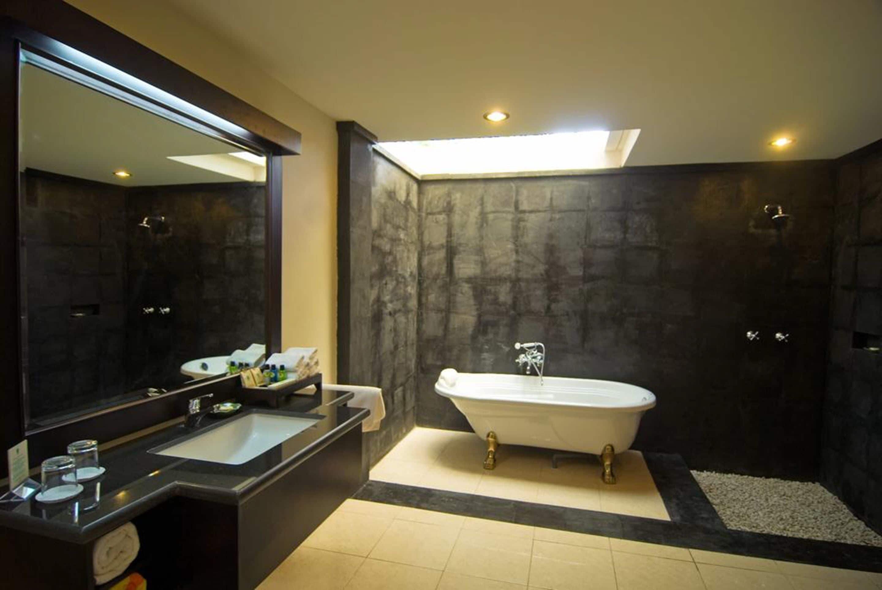 A modern bathroom with a freestanding bathtub, a large mirror, and a dark stone wall.