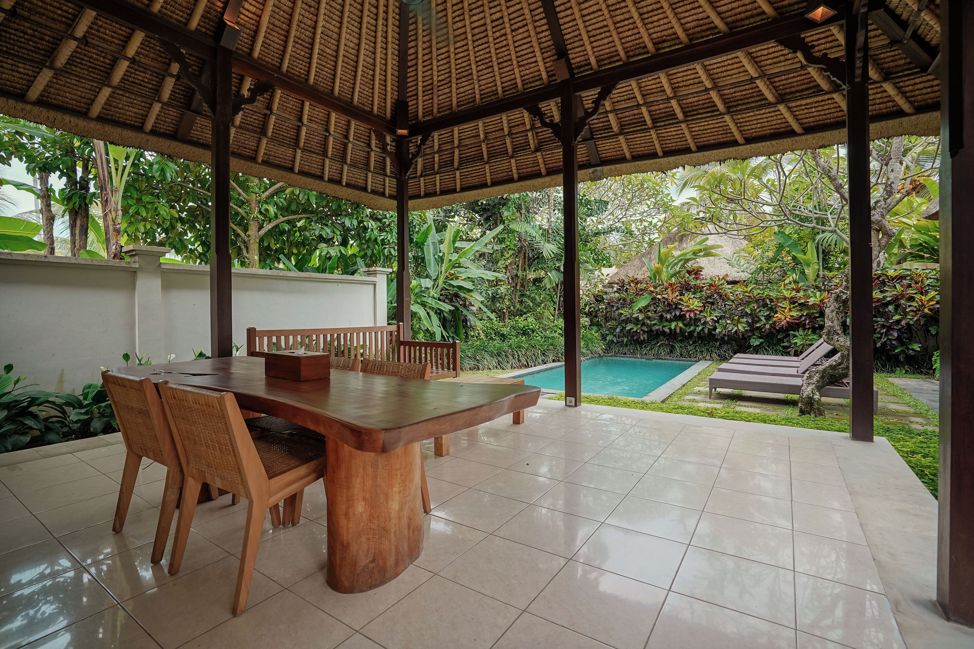A covered outdoor dining area with a pool in the background.
