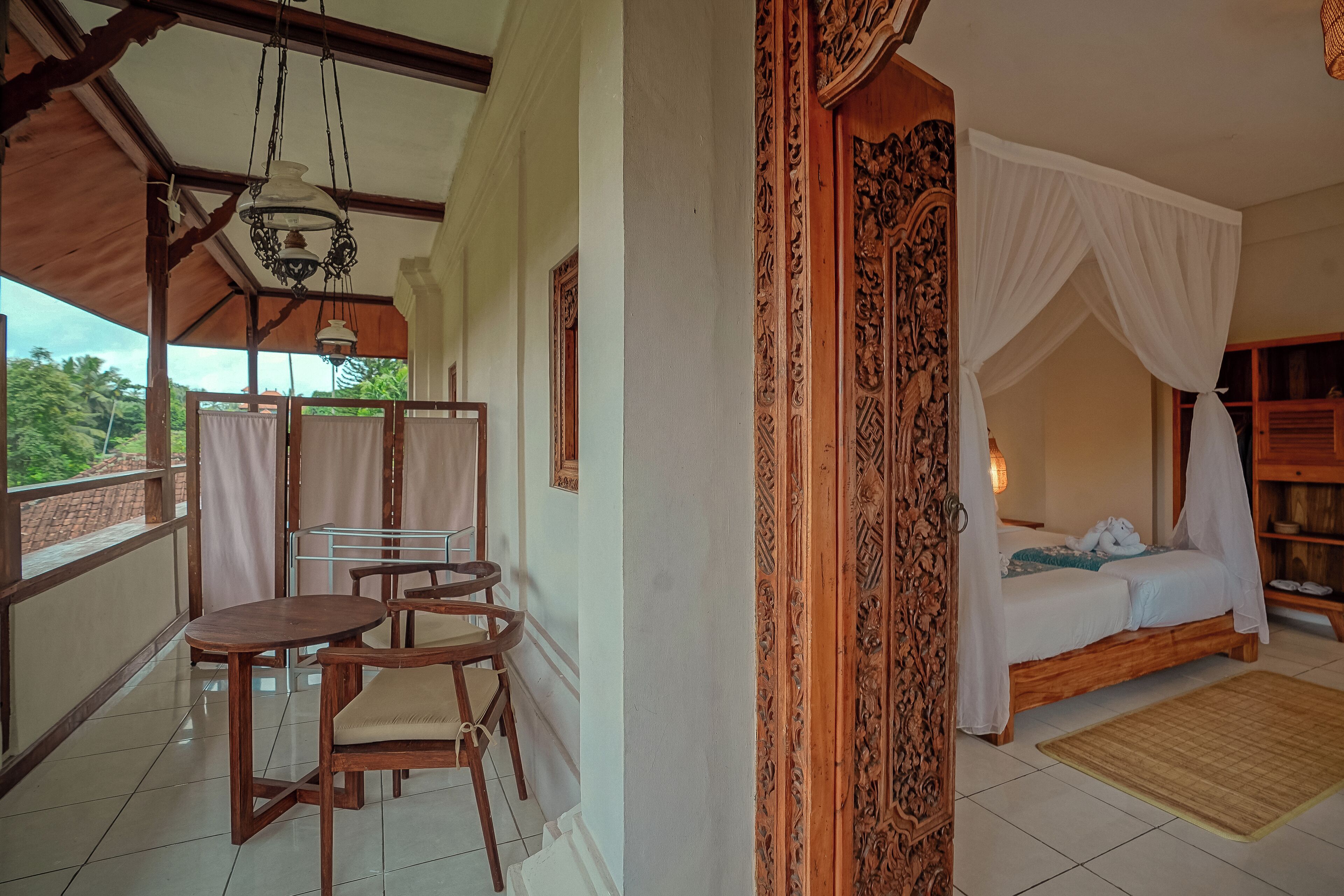 A room with a bed, a table, chairs, and a balcony with a view of greenery.