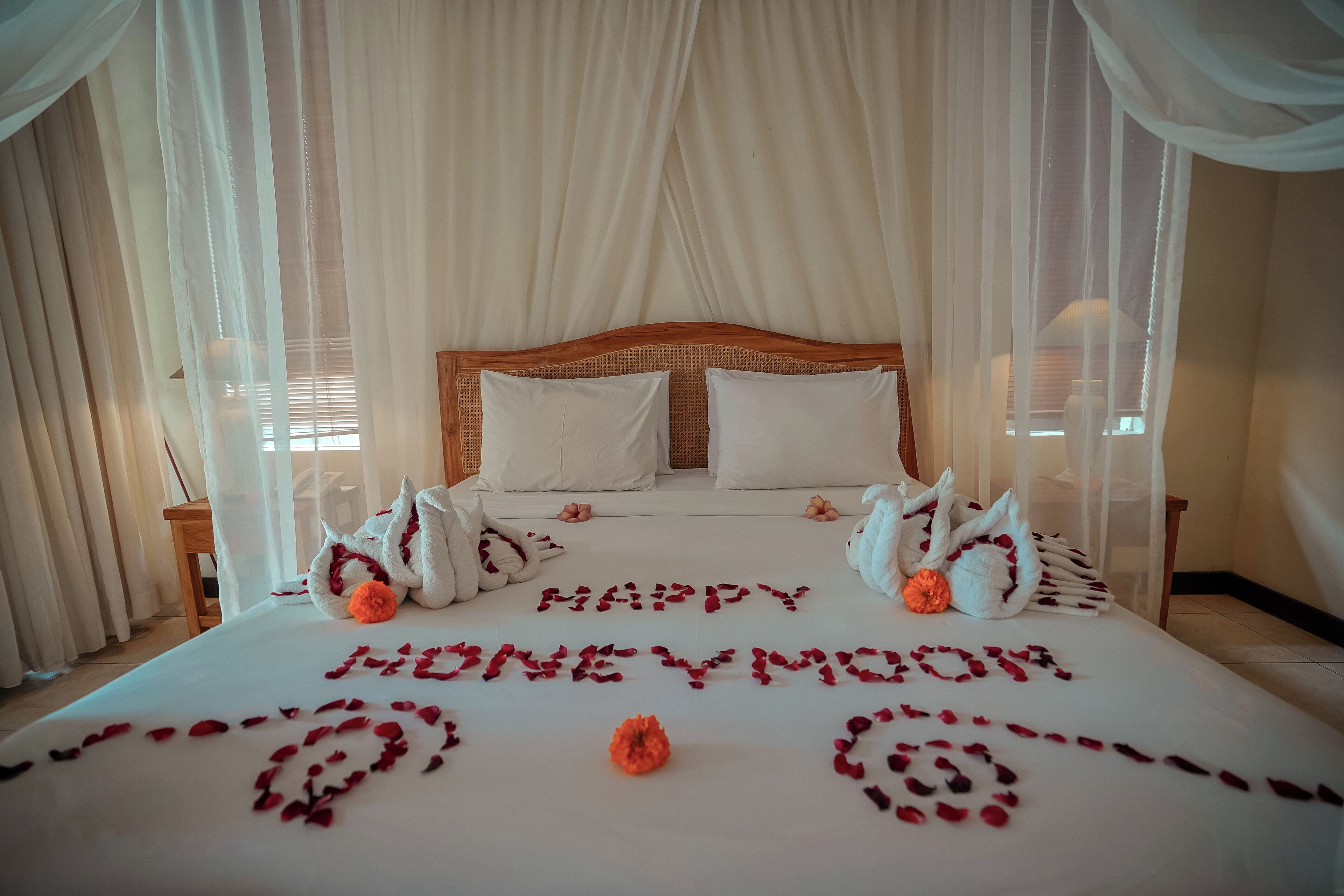 A bed with a canopy, white bedding, and rose petals spelling out "HAPPY HONEYMOON."