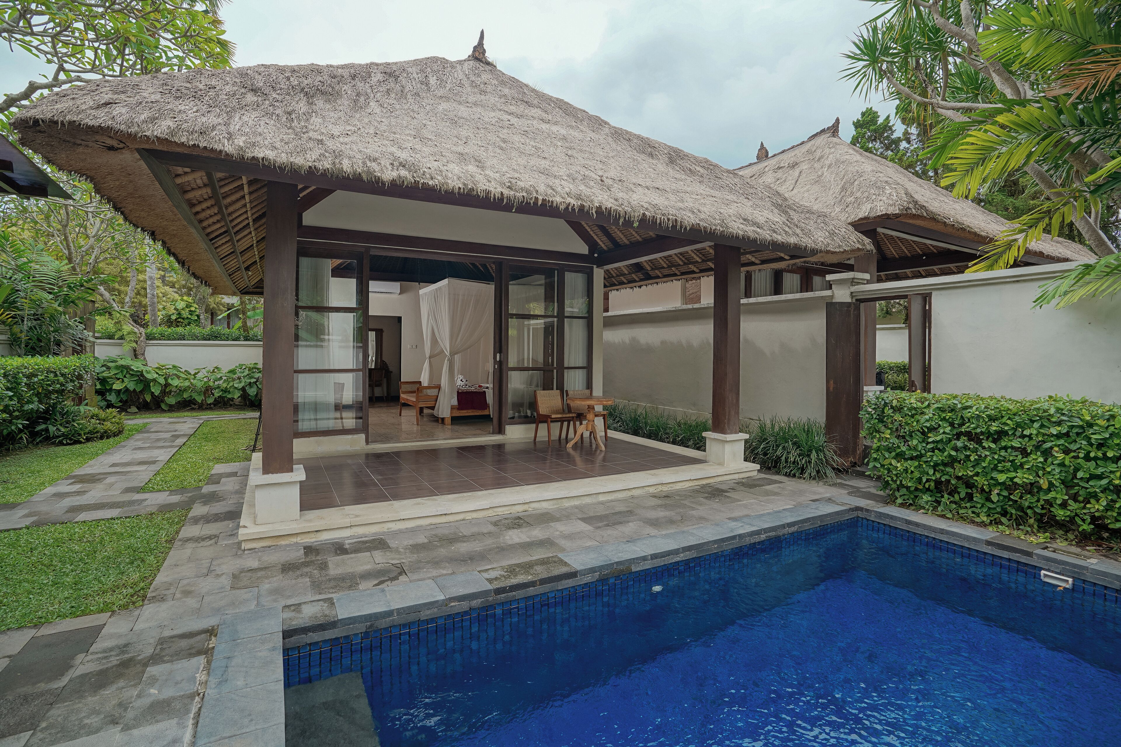 A poolside area with a thatched roof structure, a glass-enclosed room, and a swimming pool.