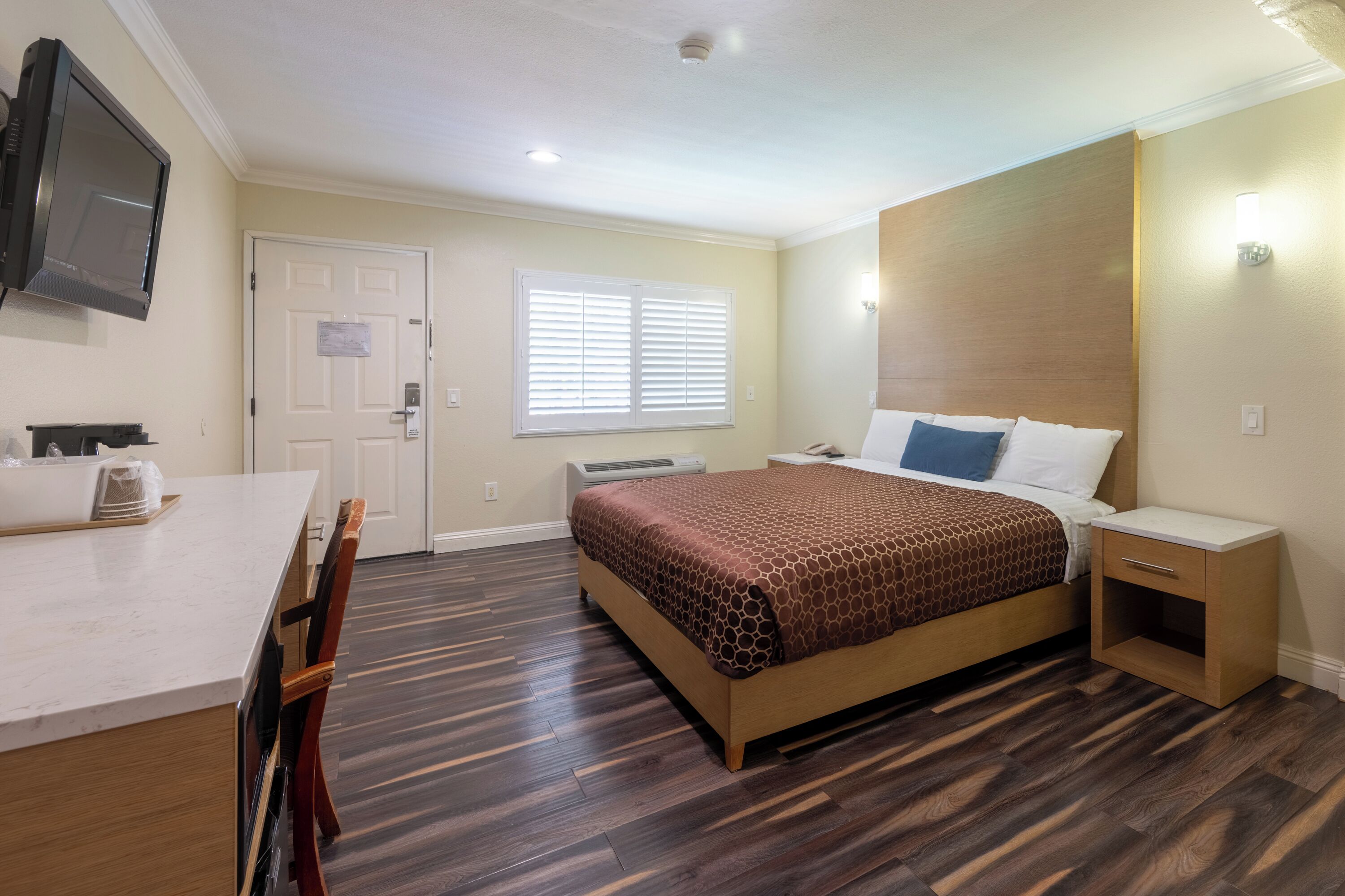 Une chambre d’hôtel équipée d’un lit, d’un bureau, d’une chaise, d’une télévision et d’une fenêtre avec des stores.