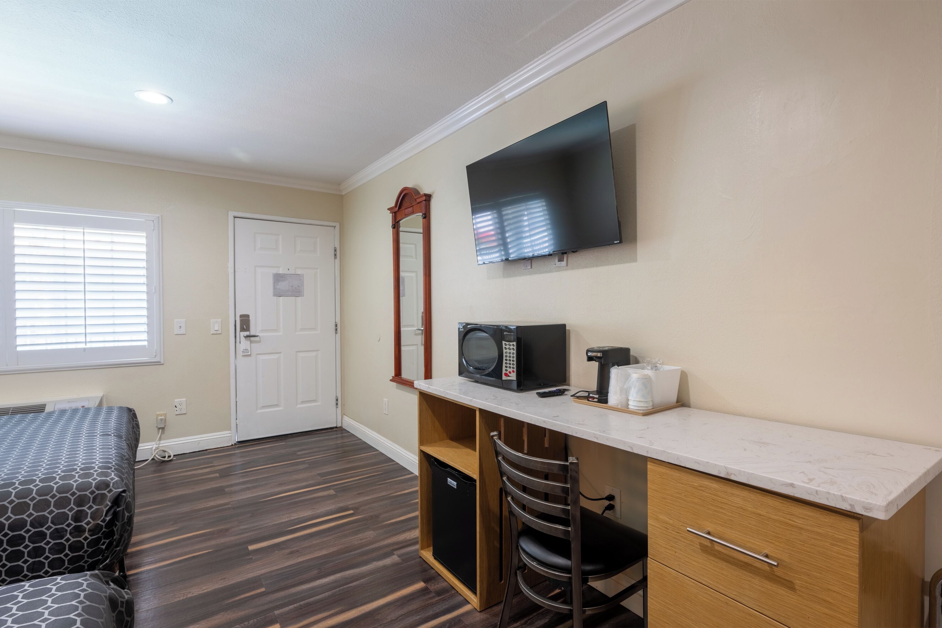 A compact room with a bed, a desk with a microwave, a chair, a television, and a door.