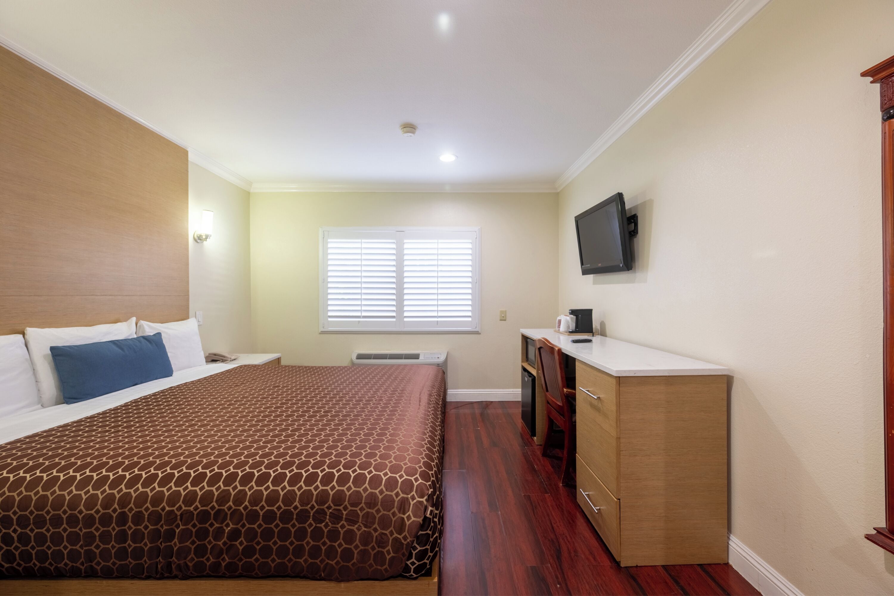 Une chambre à coucher comprenant un lit, un bureau, une télévision et une fenêtre avec des stores.