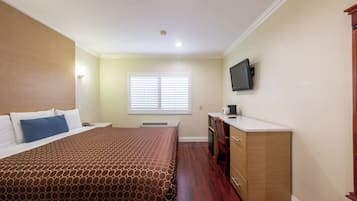 Une chambre à coucher comprenant un lit, un bureau, une télévision et une fenêtre avec des stores.