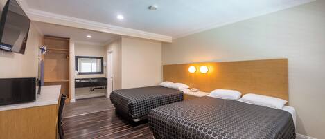 A hotel room with two beds, a desk, a TV, and a bathroom.