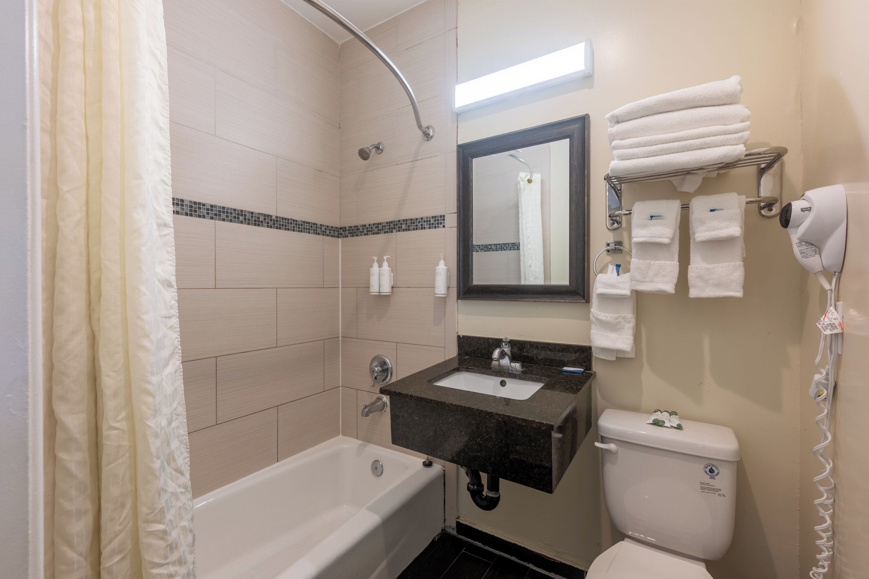 A bathroom with a bathtub, sink, and toilet. There are towels and toiletries on the sink and a hairdryer on the wall.