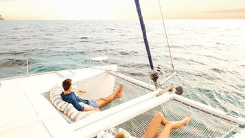 A sailboat with two people lying on deck chairs, facing the sea.