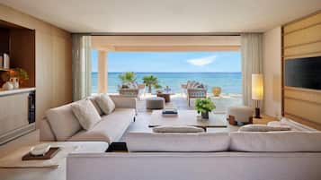 A modern living room with a sofa, coffee table, and chairs, a TV, and a view of the ocean.