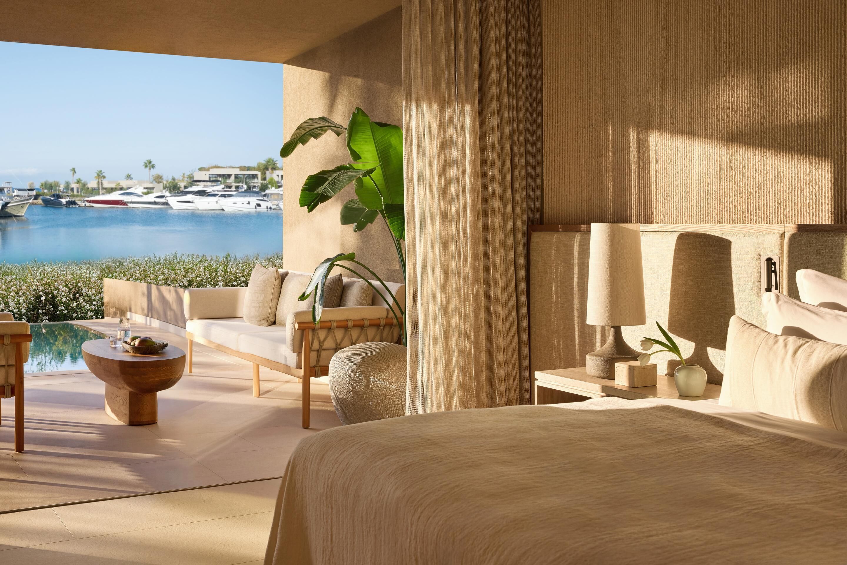 Una habitación de hotel moderna con una cama grande, un sofá, una mesita de centro y vistas a un puerto deportivo.