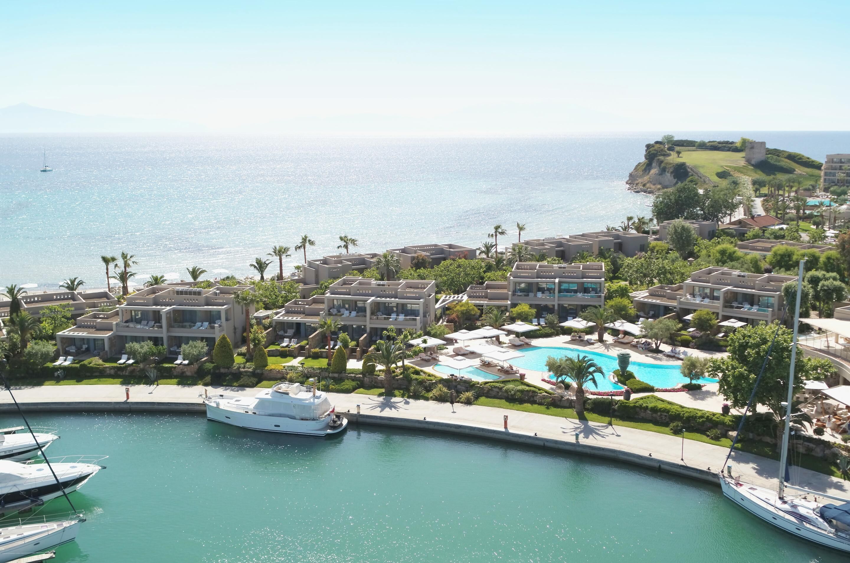 Un complejo turístico costero con varios edificios hoteleros, una piscina y yates amarrados en un puerto deportivo.