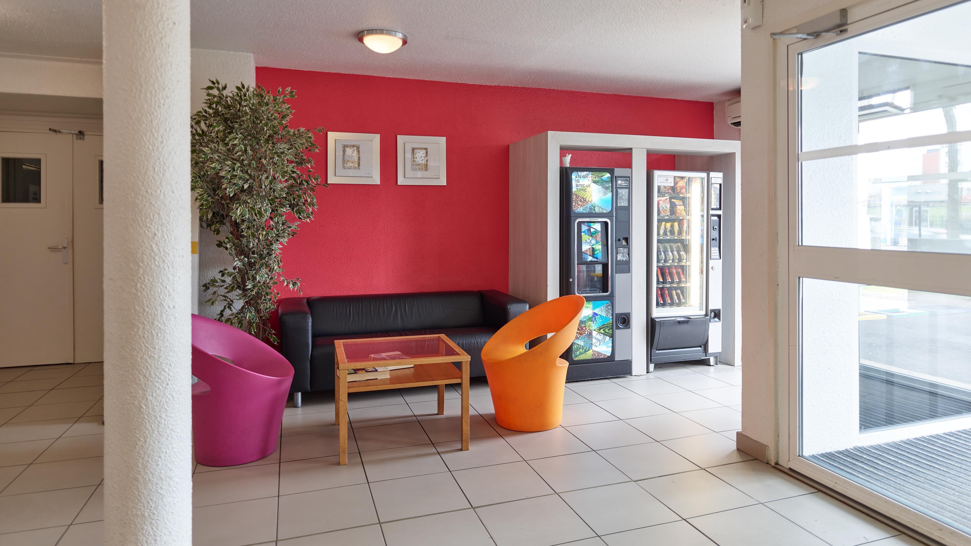 A room with a red wall, a black leather sofa, a wooden coffee table, a pink chair, and a vending machine.