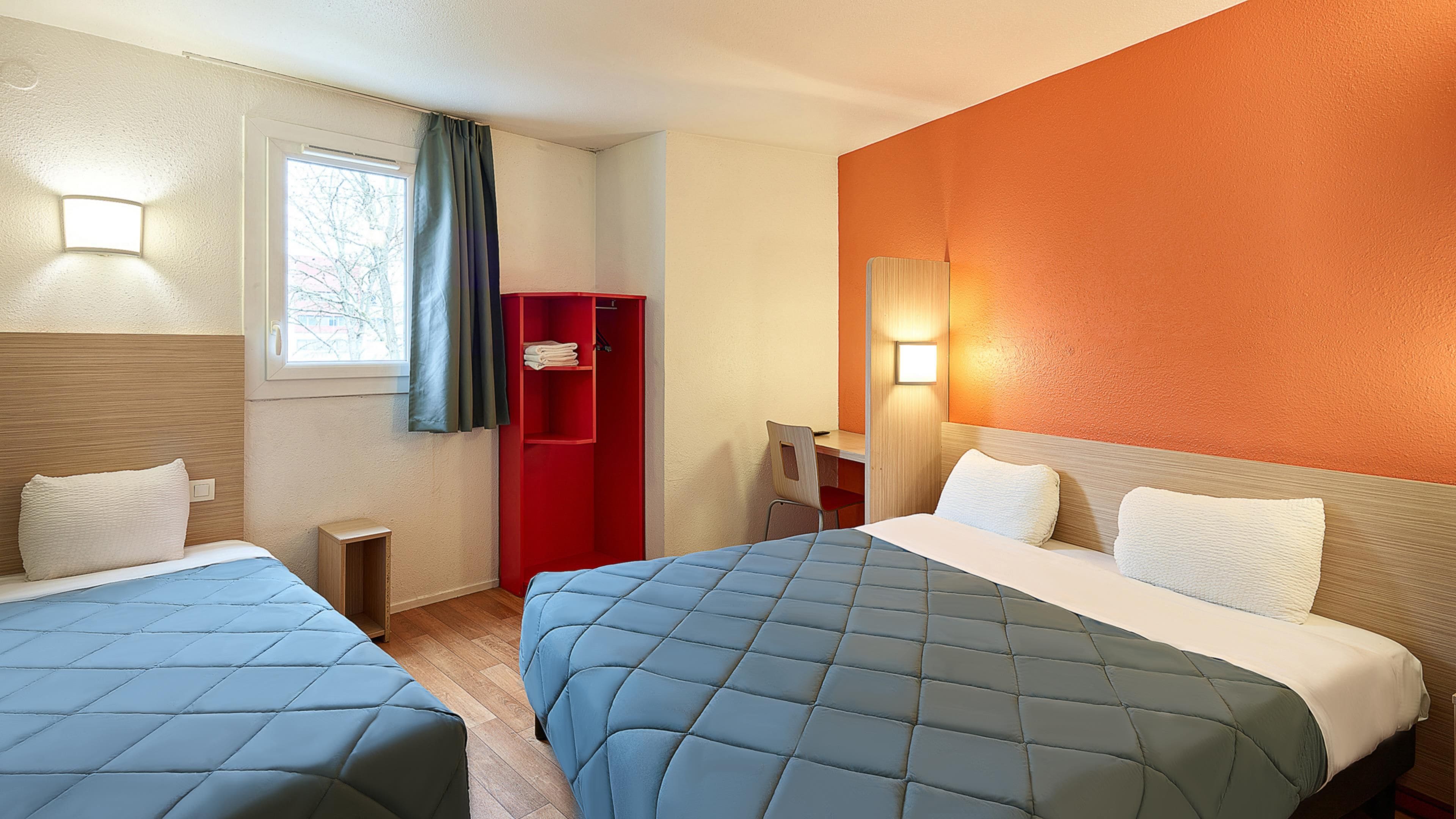 Une chambre d’hôtel avec deux lits, un bureau, une chaise et une armoire rouge.