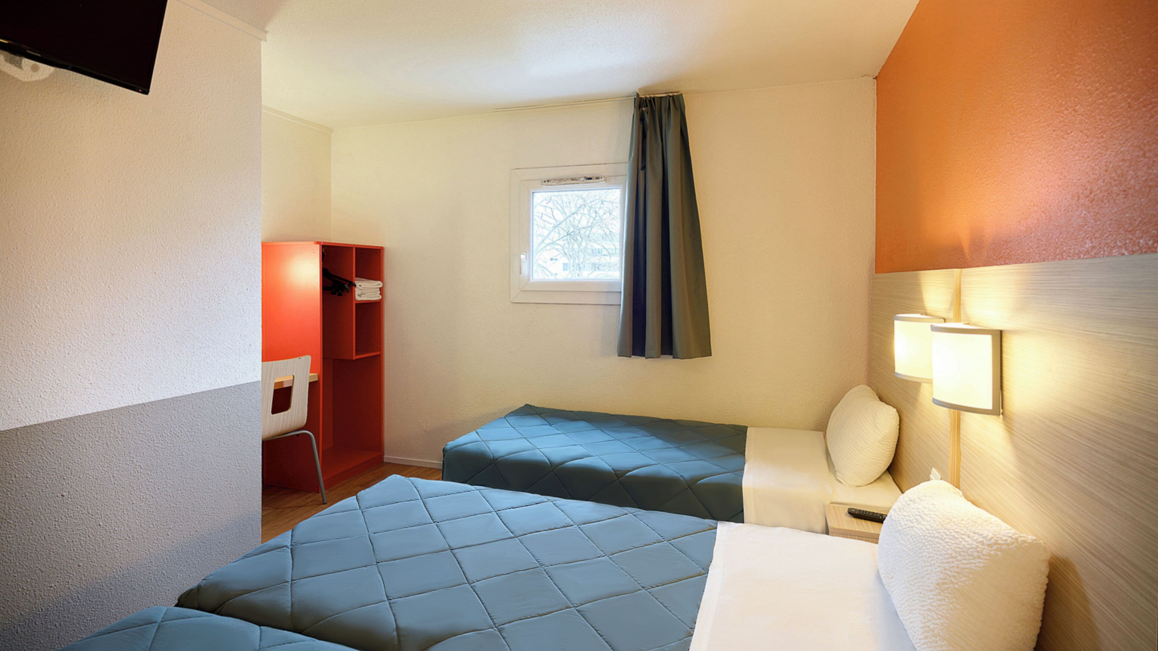 A hotel room with two beds, a desk, a chair, a wardrobe, and a window with curtains.