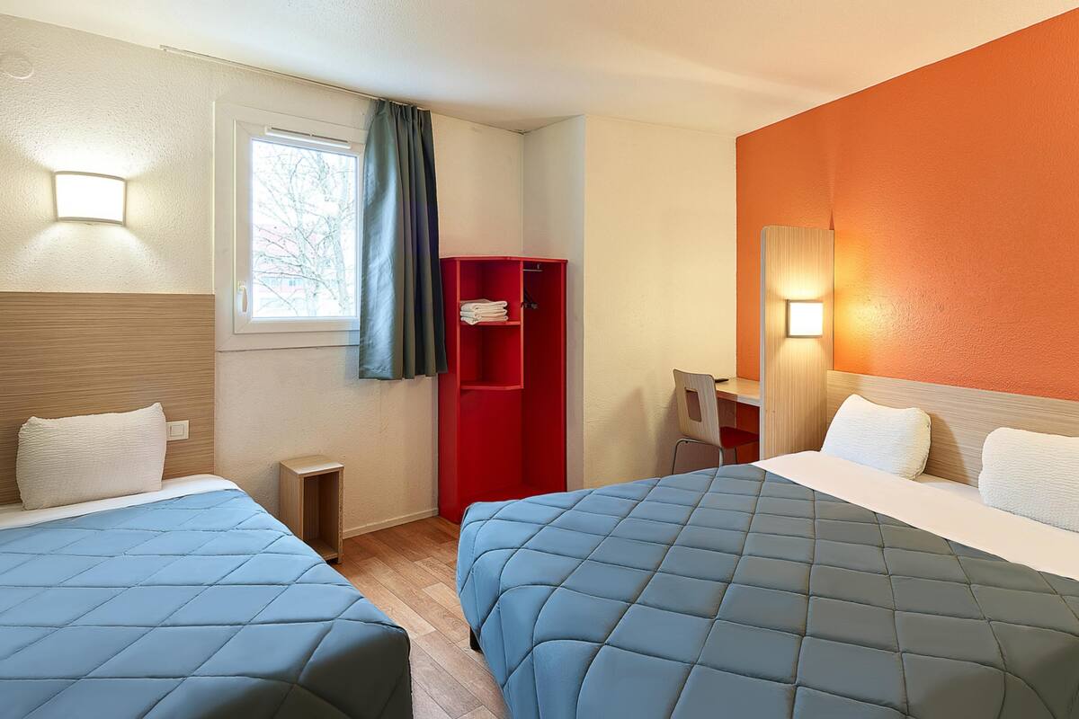A hotel room with two beds, a desk, a chair, and a red wardrobe.