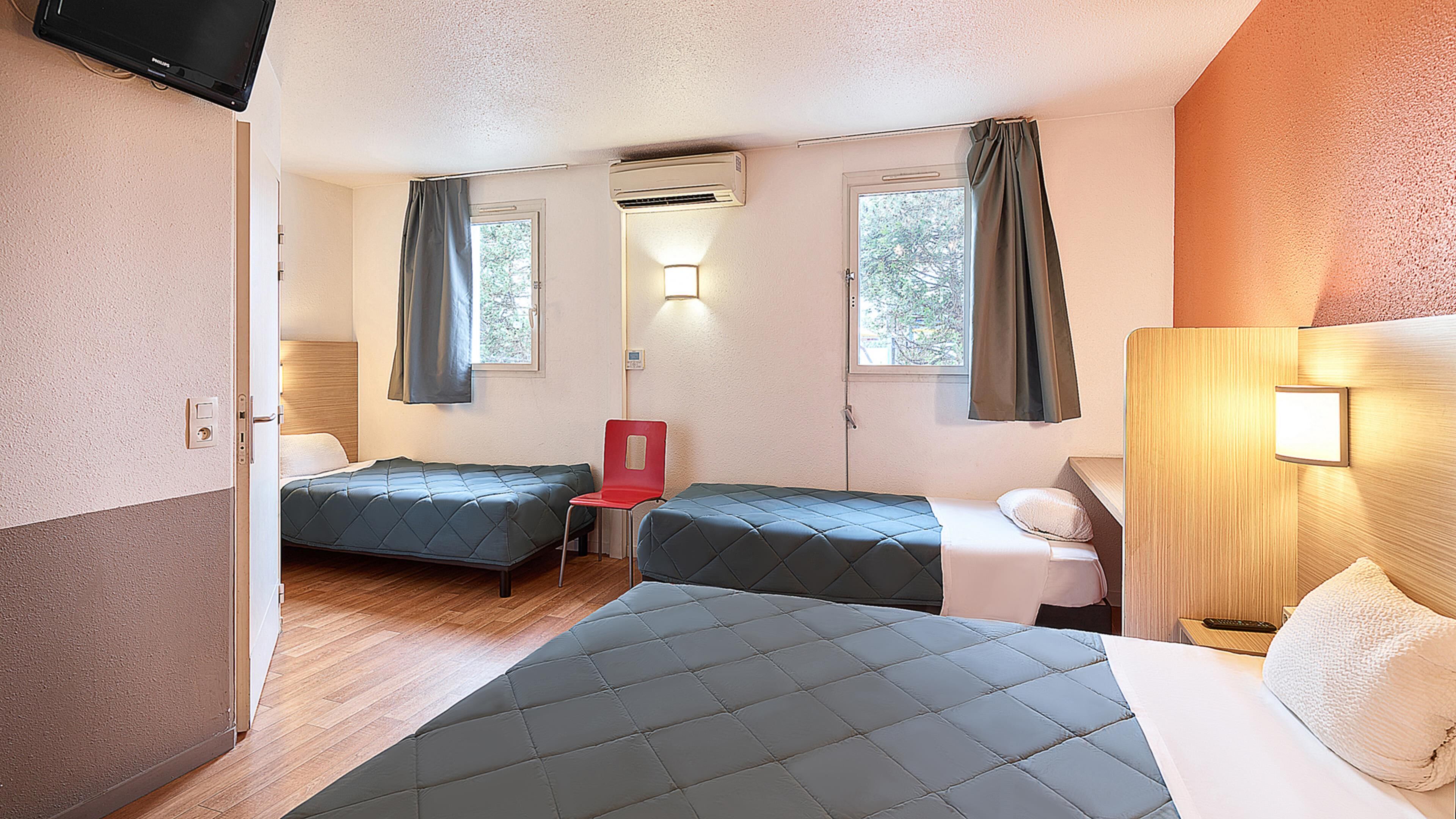 A room with two beds, a chair, a TV, and a window with curtains.