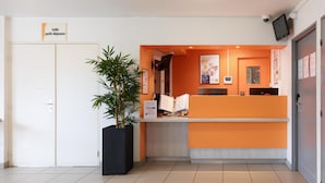 A reception desk with a sign indicating a small waiting area, a potted plant, a computer monitor, and a security camera.