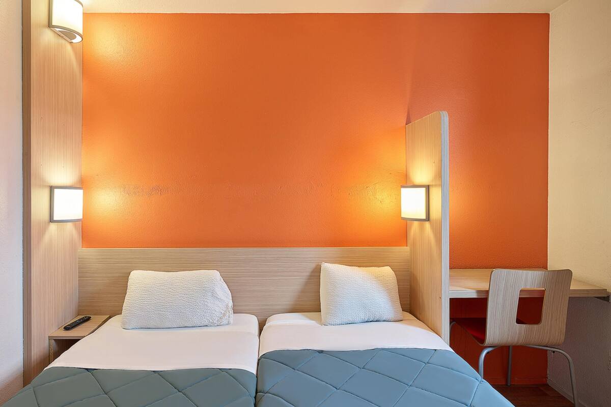 A hotel room with two beds, a desk, and a chair.