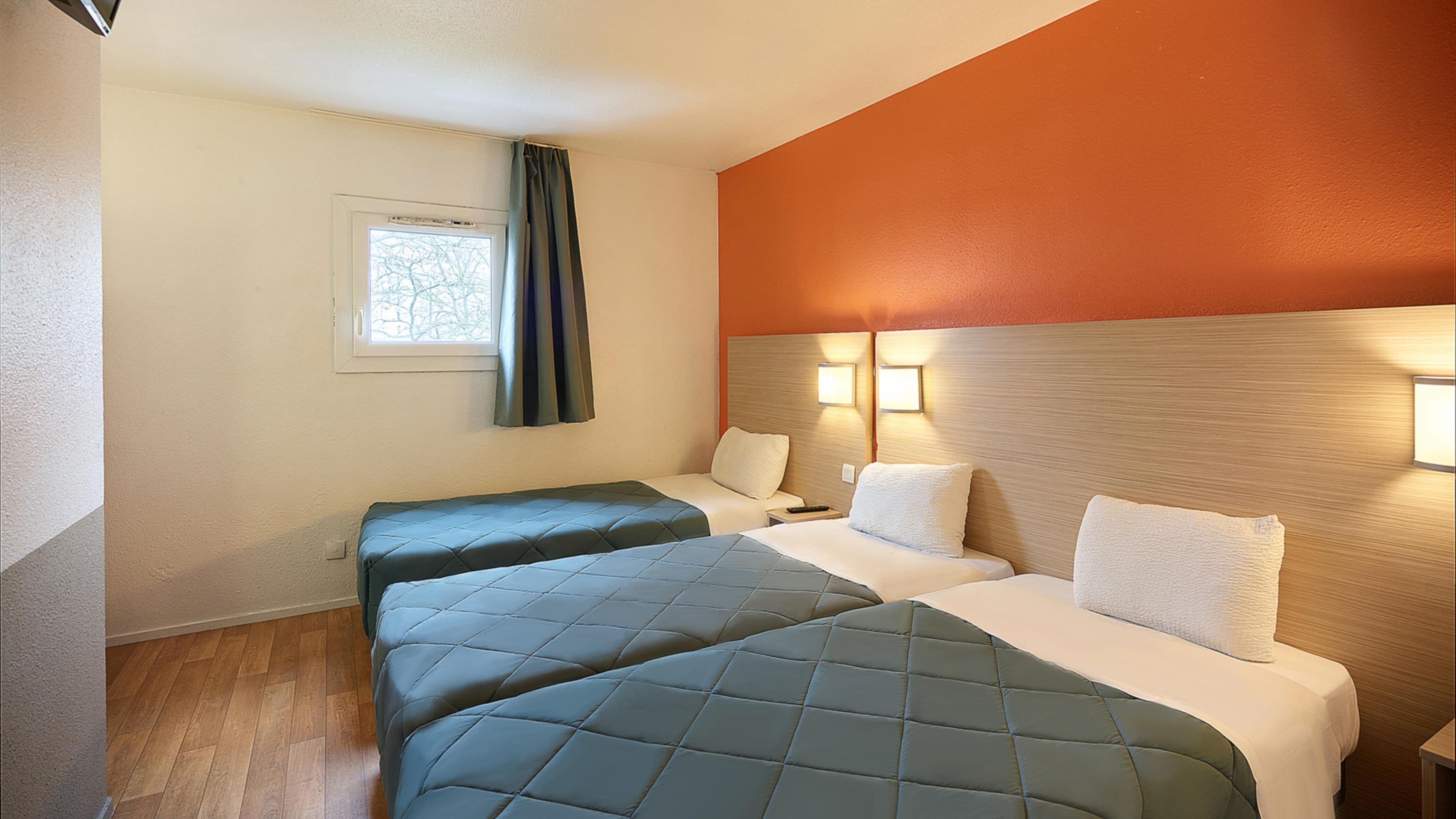 Habitación de hotel con dos camas, una ventana con cortinas, una lámpara de pared y suelo de madera.