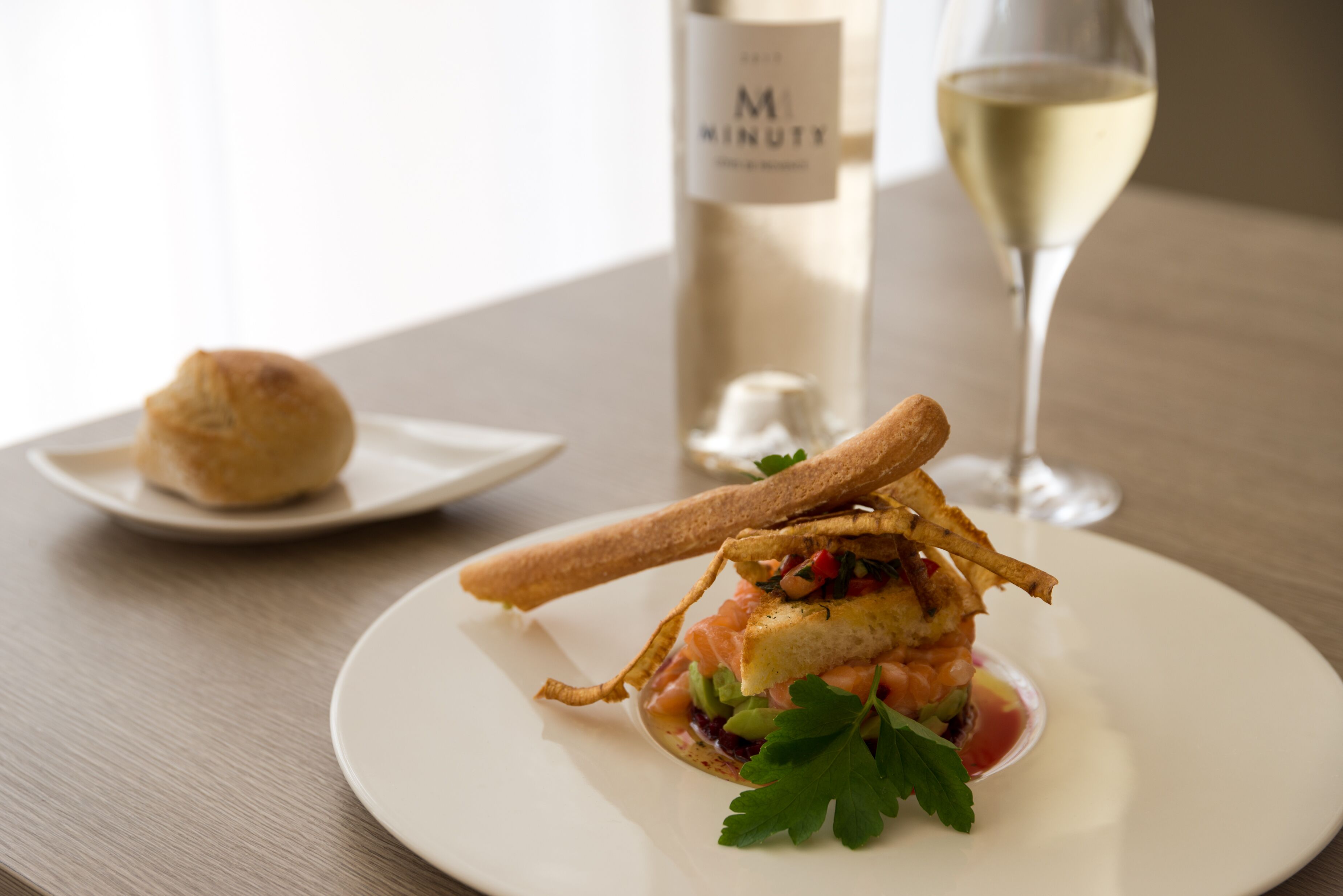 A plate of food with a glass of white wine and a bottle in the background.
