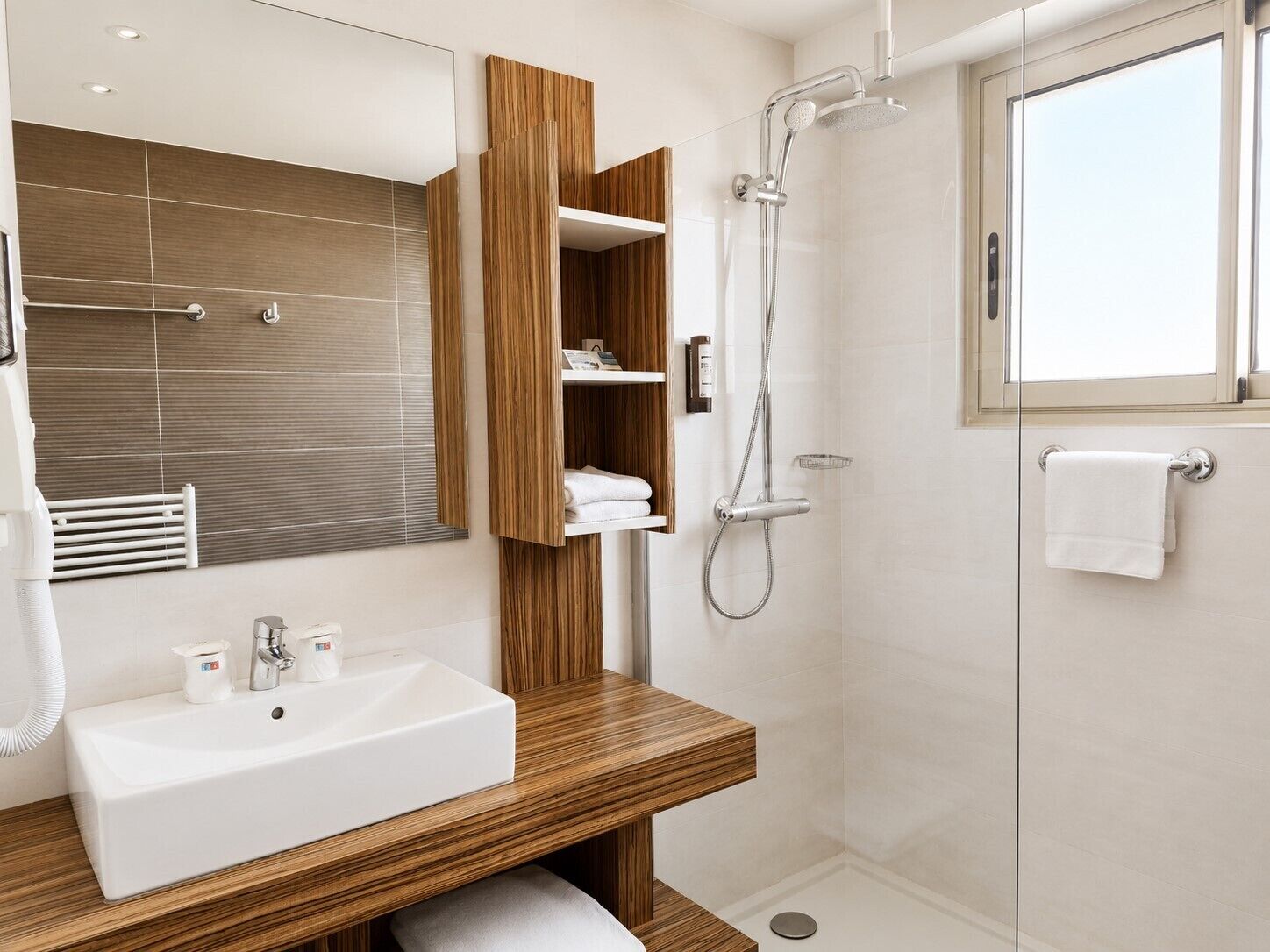 Un baño moderno con un lavamanos blanco, tocador de madera, cabina de ducha de vidrio y un espejo grande.