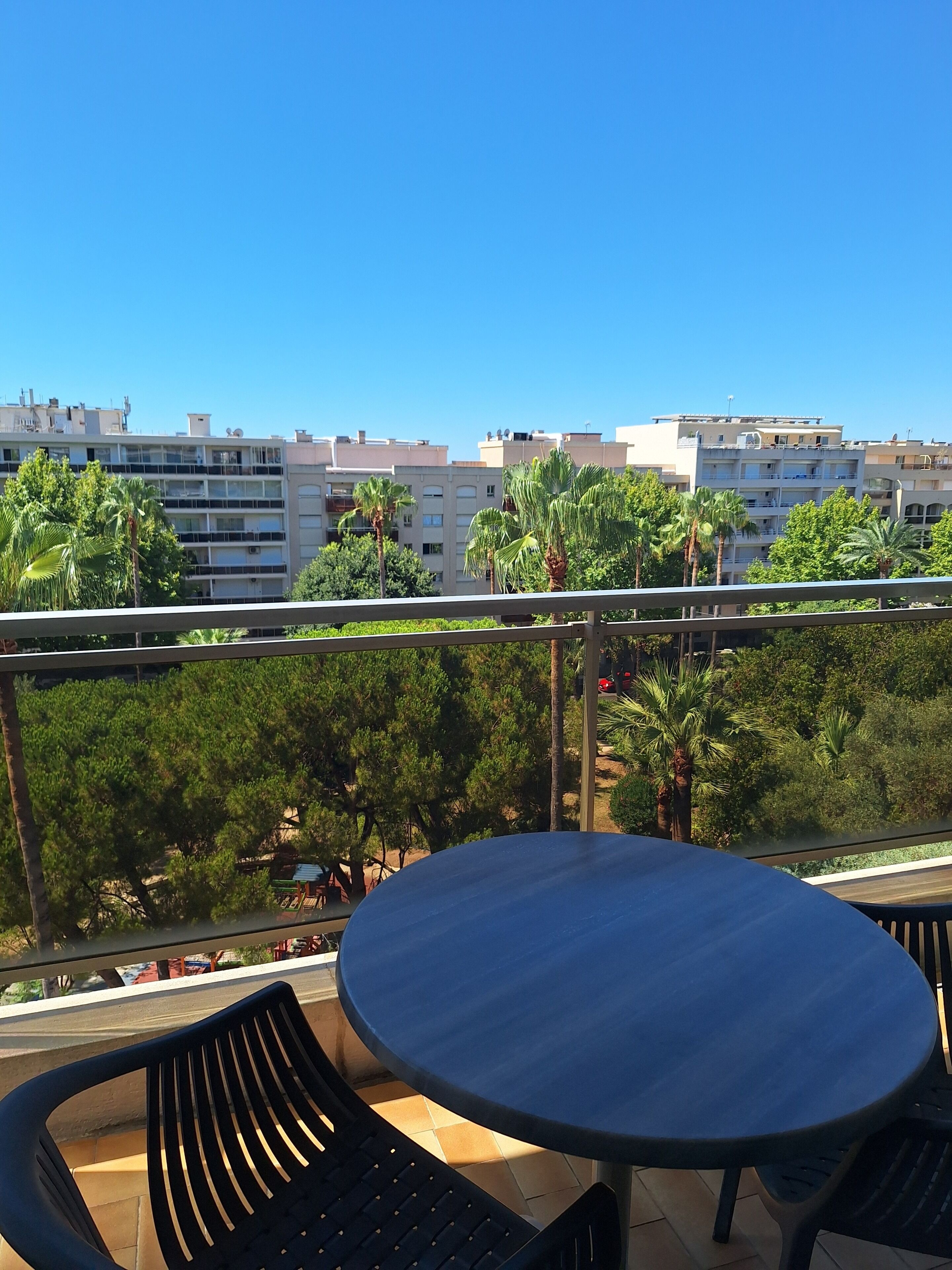 A balcony with a round table and chairs, overlooking a residential area with buildings and trees.