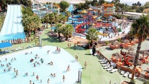 A water park with multiple slides and pools, surrounded by palm trees and shaded areas.