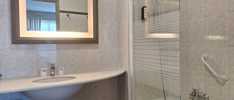 Une salle de bain équipée d’un lavabo, d’un miroir et d’une douche en verre avec un pommeau de douche amovible.