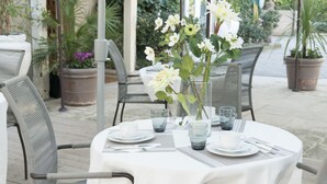 An outdoor dining area with round tables, chairs, and potted plants. - Hôtel ERMITAGE (Les Angles)