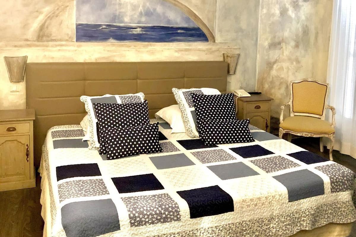 A bedroom with a large bed, a view of the sea through a window, and a chair.
