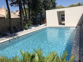 Una piscina al aire libre, sombrillas, sillones reclinables de piscina