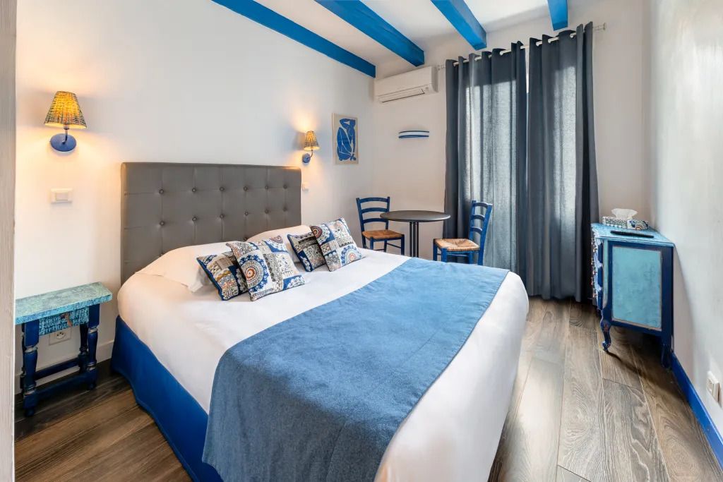 Un dormitorio con cama, mesitas de noche, una silla, una mesita pequeña y una cortina.