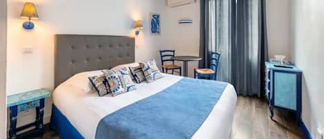 Un dormitorio con cama, mesitas de noche, una silla, una mesita pequeña y una cortina.
