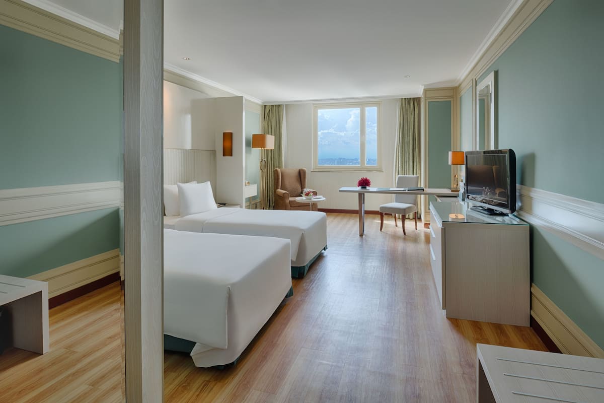 Une chambre d’hôtel avec deux lits, un bureau, une chaise, une télévision et une fenêtre donnant sur un beau paysage.