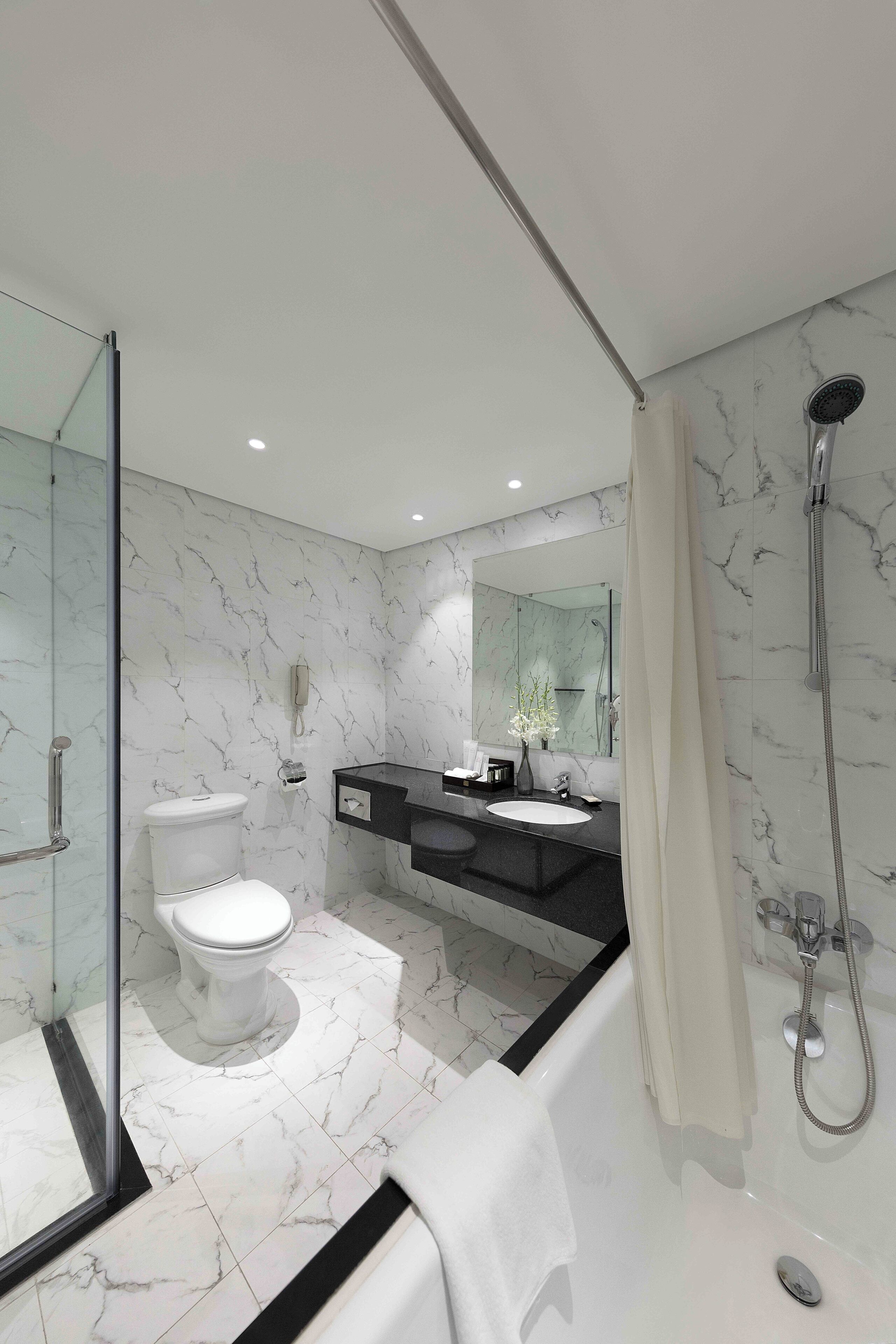 A modern bathroom with a glass shower enclosure, a white toilet, a black vanity, and a marble floor.