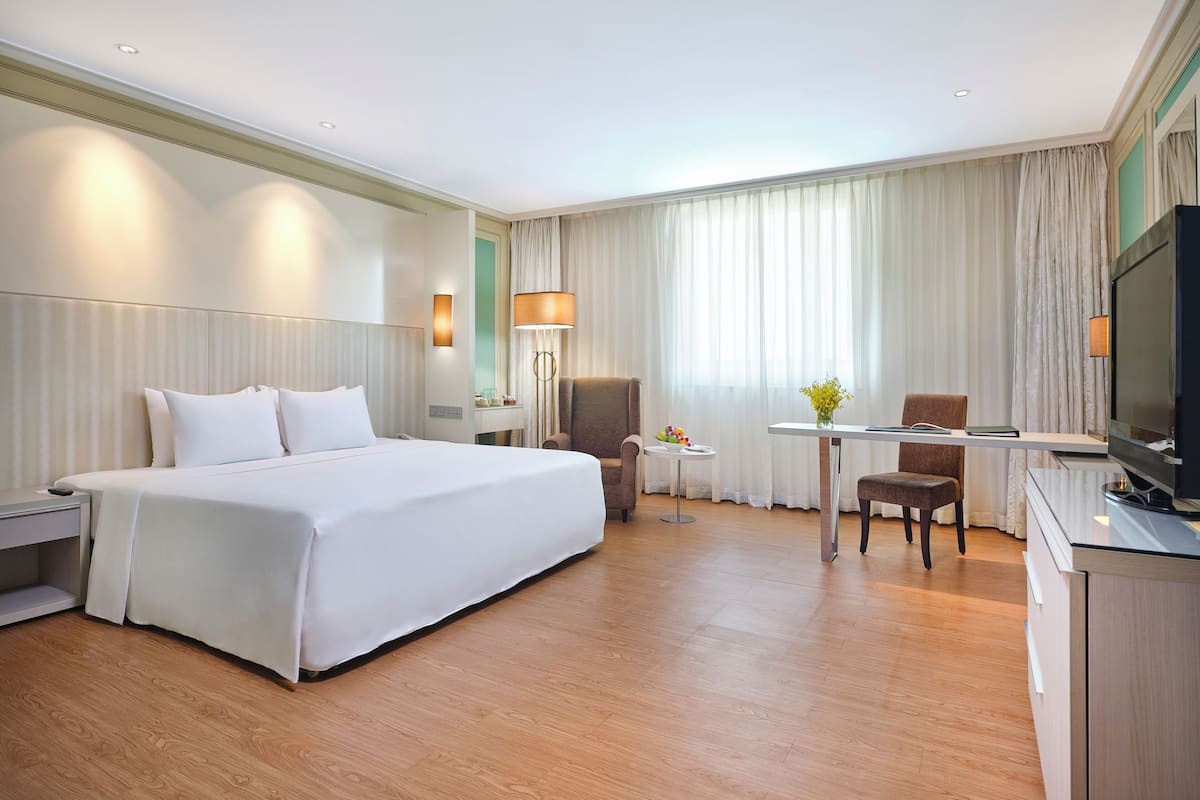 Une chambre d’hôtel avec un grand lit, un bureau avec une chaise, une télévision et une petite table avec une lampe.