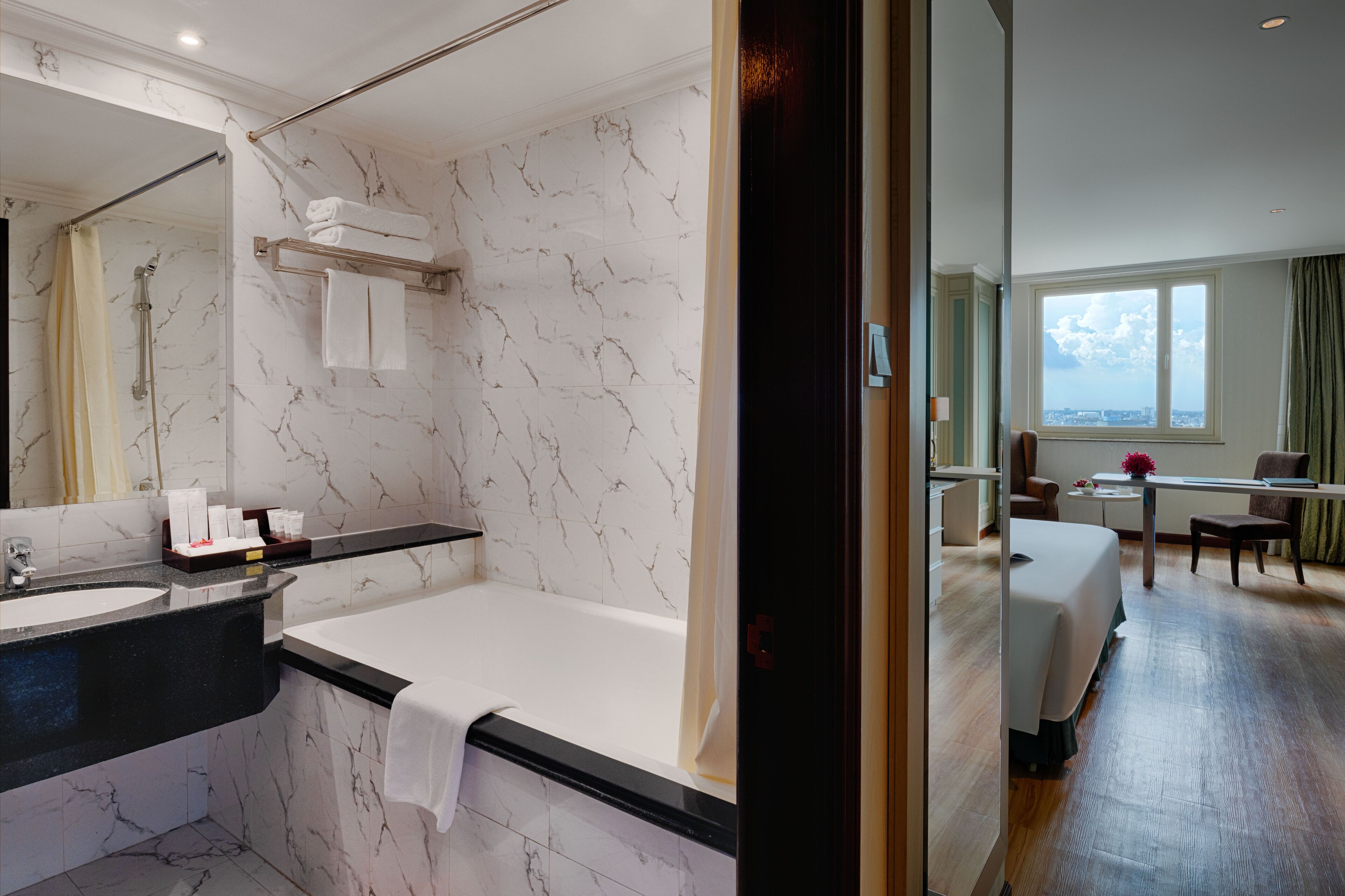 A modern bathroom with a marble wall, a bathtub, and a vanity with a mirror.