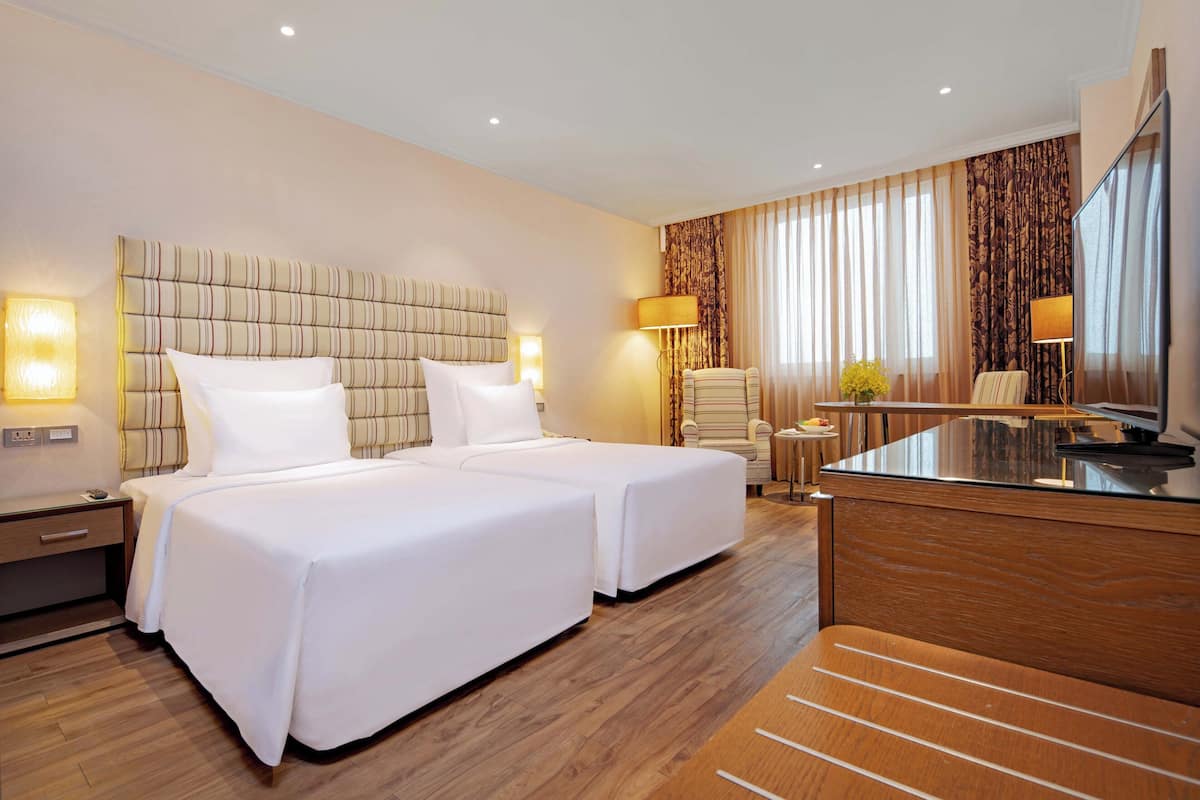 Une chambre d’hôtel avec deux lits, un bureau, une chaise et un grand miroir.