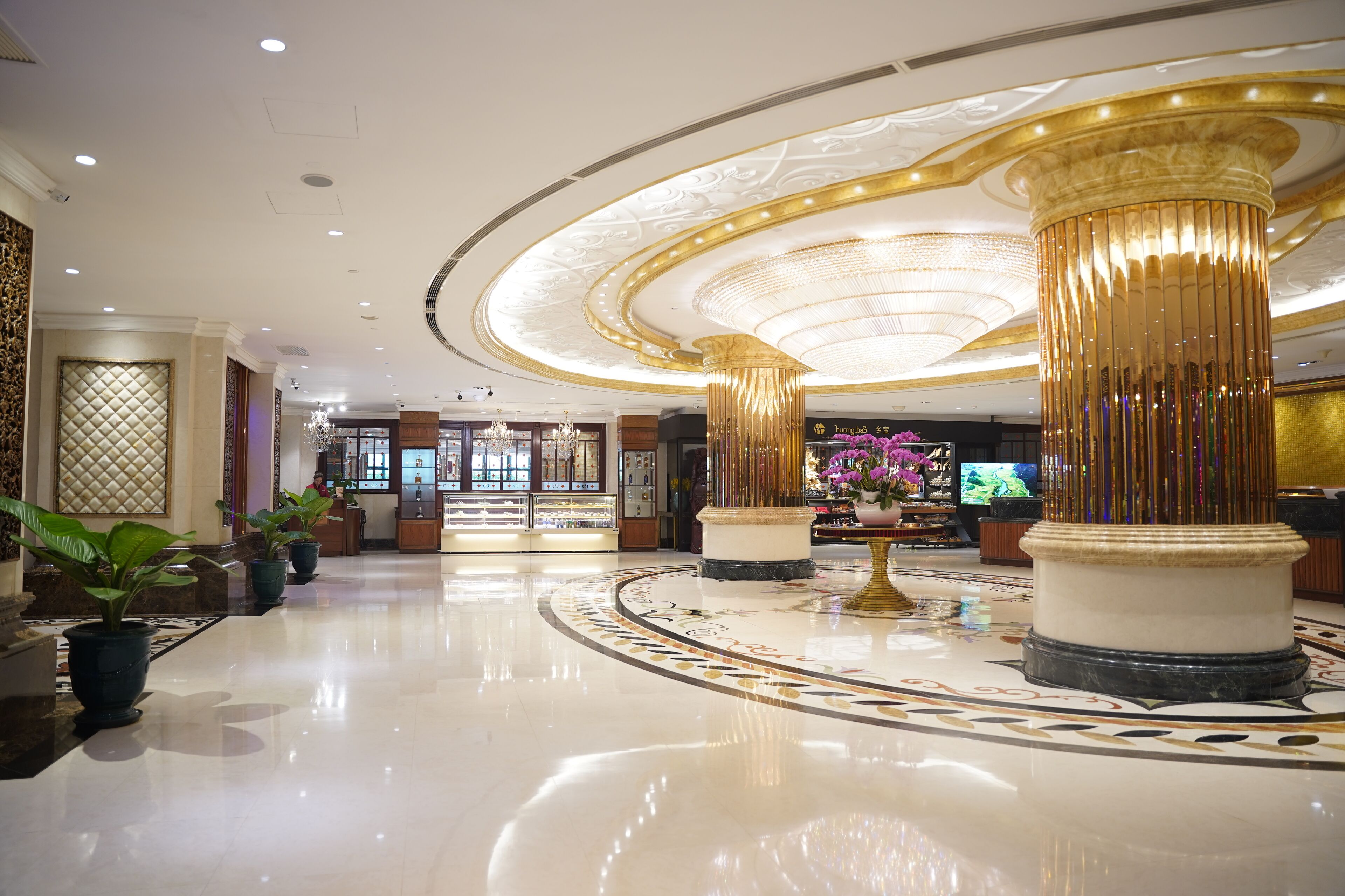 A spacious lobby with a polished marble floor, large decorative columns, and a chandelier.
