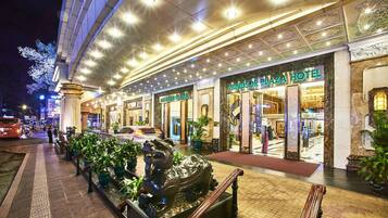 A hotel entrance with a grand facade, a staircase, and potted plants along the walkway.