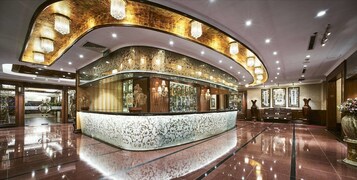 A lobby with a curved reception desk, ornate wall decorations, and a polished marble floor.