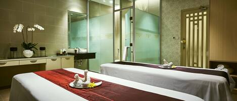 A hotel room with two beds, a bathroom with a glass shower enclosure, and a vanity with a mirror and toiletries.