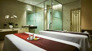Une chambre d’hôtel avec deux lits, une salle de bain dotée d’une douche à parois de verre et d’un meuble-lavabo avec un miroir et des articles de toilette.