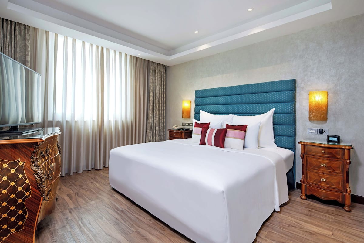 Une chambre d’hôtel avec un grand lit, des tables de chevet en bois, une télévision et une fenêtre avec des rideaux.