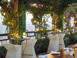 Un restaurante con terraza, mesas y sillas, y plantas colgantes.