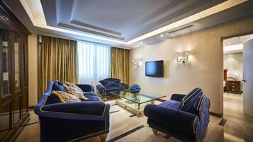 Una sala de estar lujosa con diseño moderno, que presenta un televisor de pantalla plana grande, elegantes sofás azules con adornos dorados y una mesa de centro de vidrio.