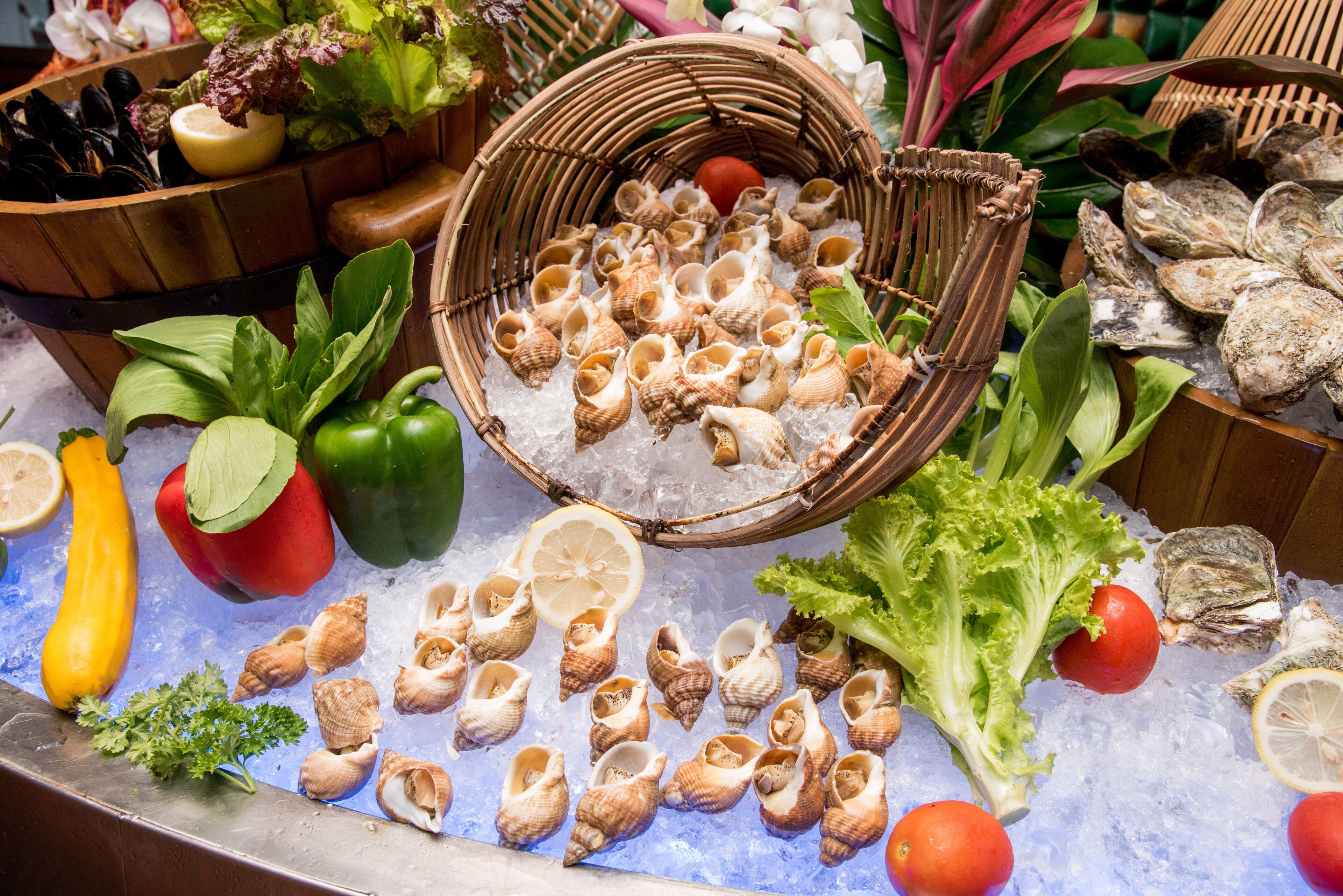 A variety of fresh seafood and vegetables displayed on ice, including mussels, oysters, and bell peppers.