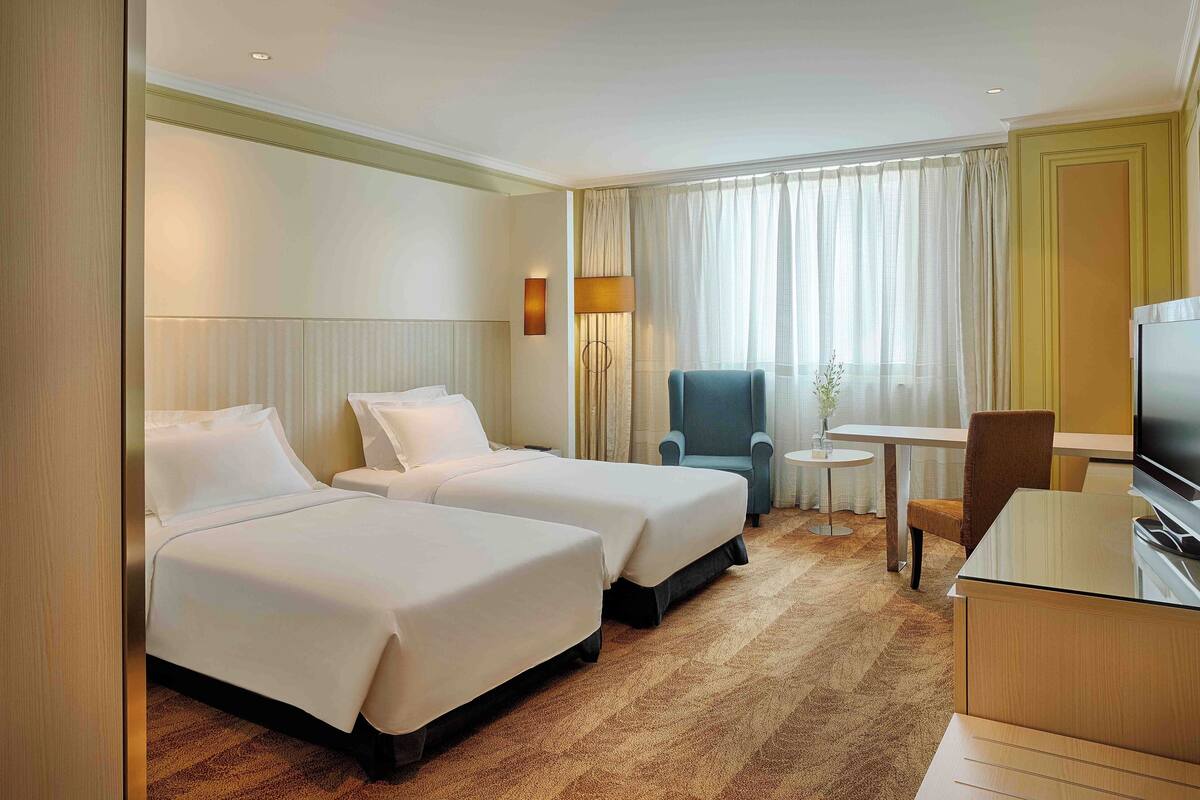 Une chambre d’hôtel avec deux lits, un bureau, une chaise, une télévision et une lampe.