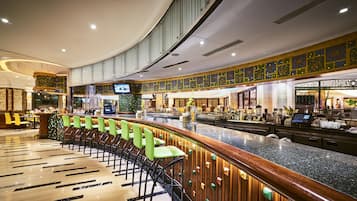 Eine moderne Bar mit einer gebogenen Theke, grünen Stühlen und einem Fernsehbildschirm.